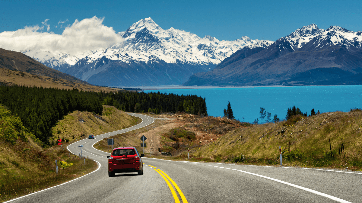 un'auto che guida lungo la strada circondata da un lago blu e montagne