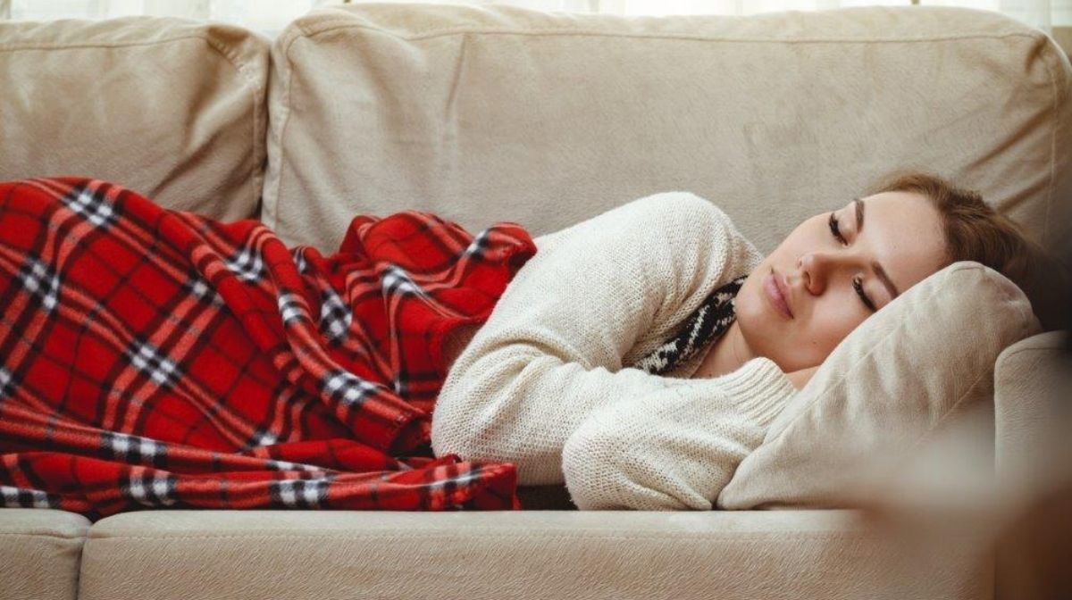 Una giovane donna sta dormendo sul divano con una coperta rossa sulle gambe 