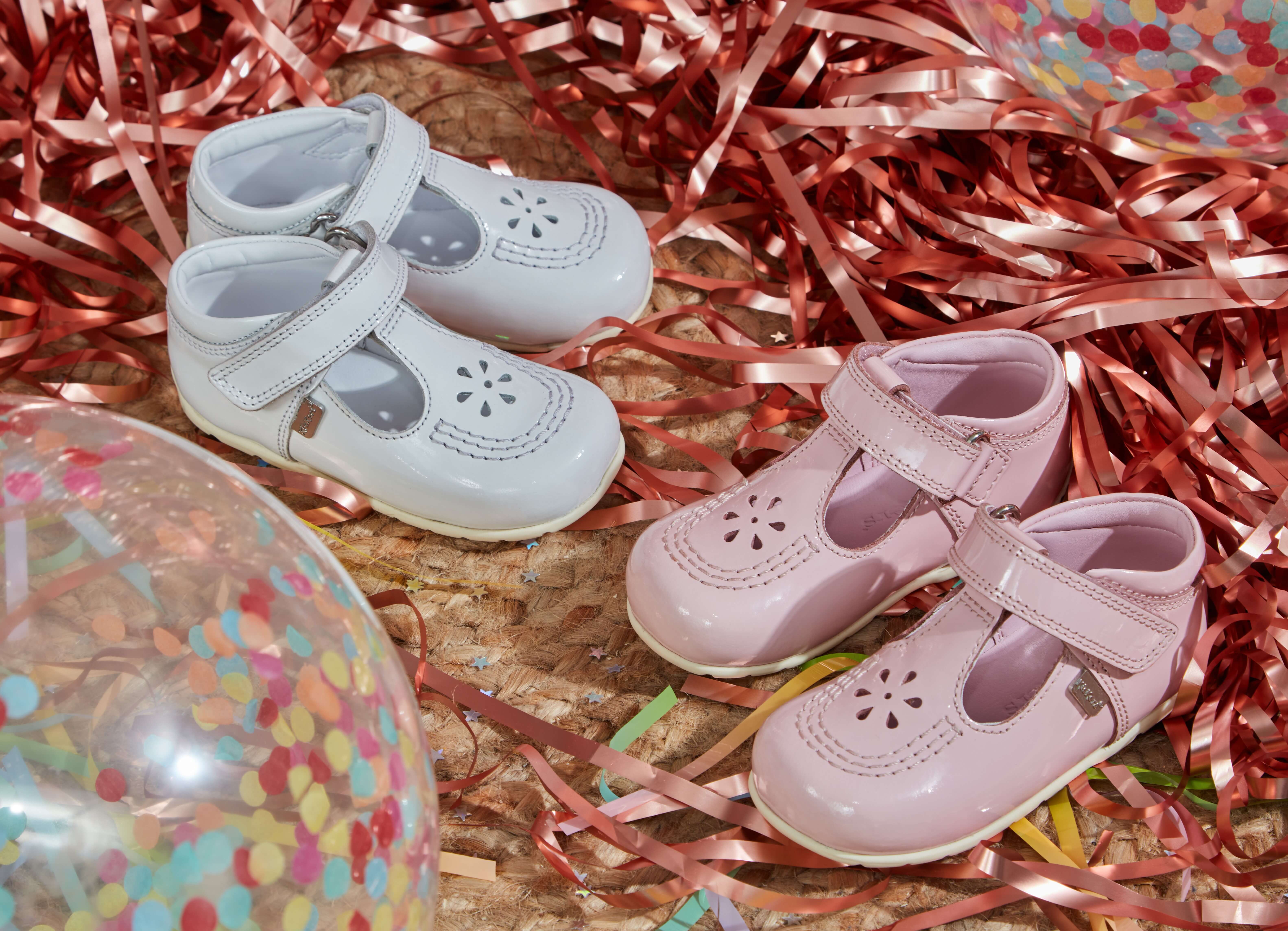 Photograph of a pink pair and white pair of children shoes, surrounded by confetti and balloons