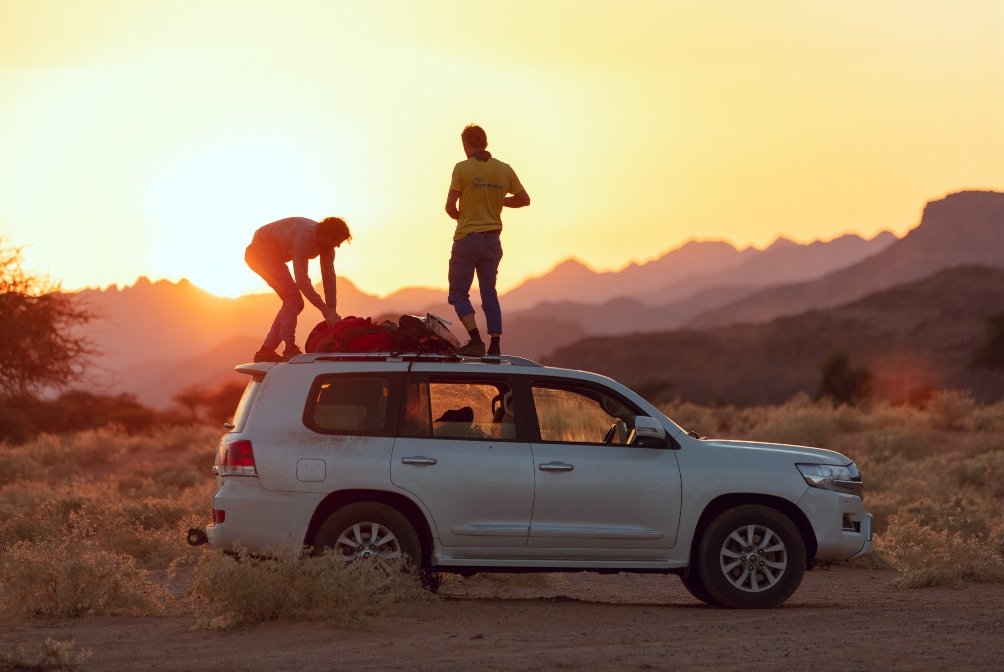Climbing duo gaze at a Bedouin sunset on top of a car