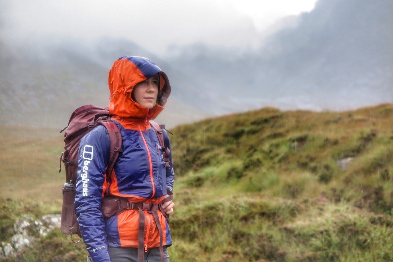Anna stands on cliff in orange and purple Berghaus waterproofs