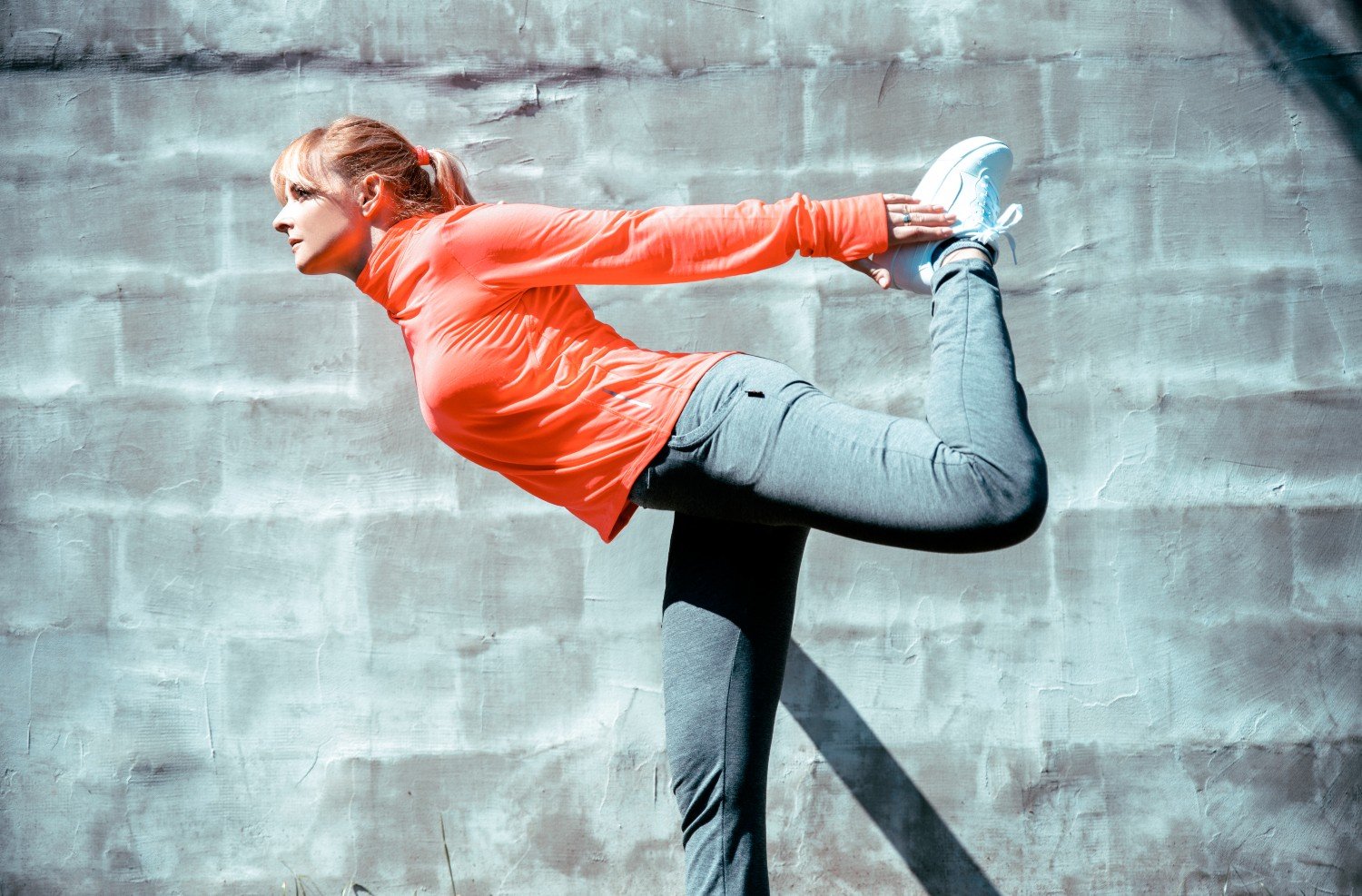 woman stretching in front of wall wearing bright gym gear 