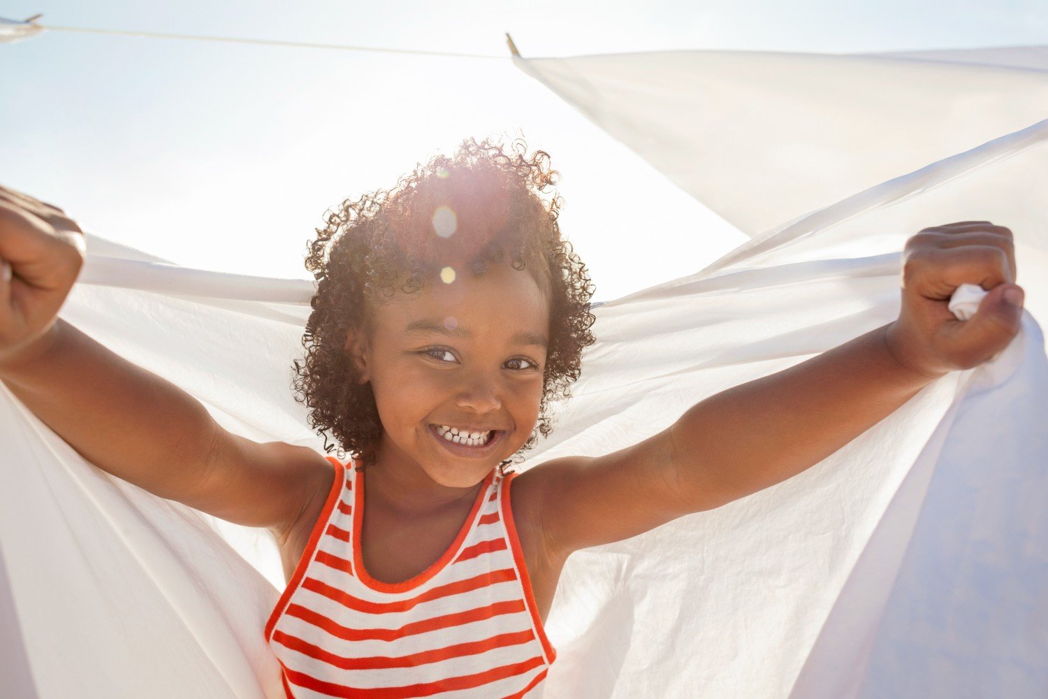 little girl plays in sunshine with washing line sheet 