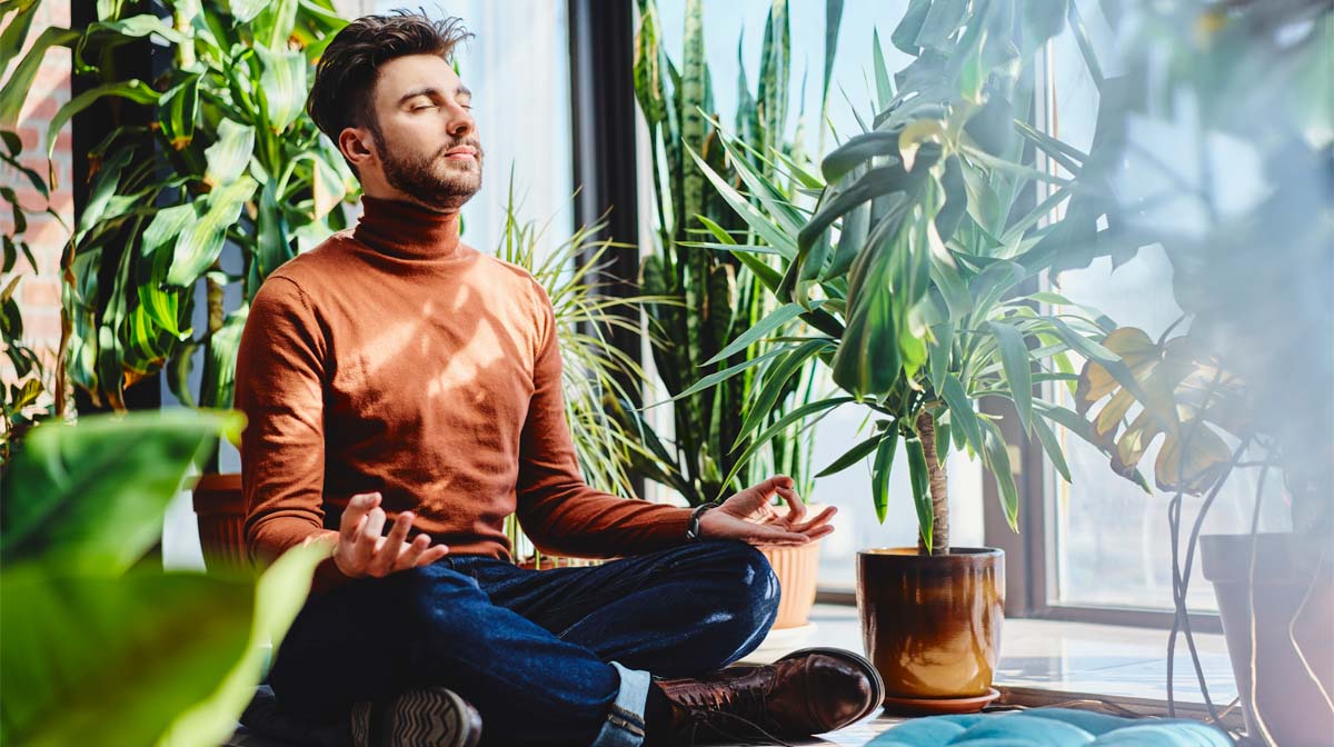man in sitting meditation pose surrounded by plants