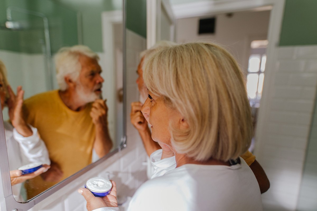 senior couple apply face cream in mirror 