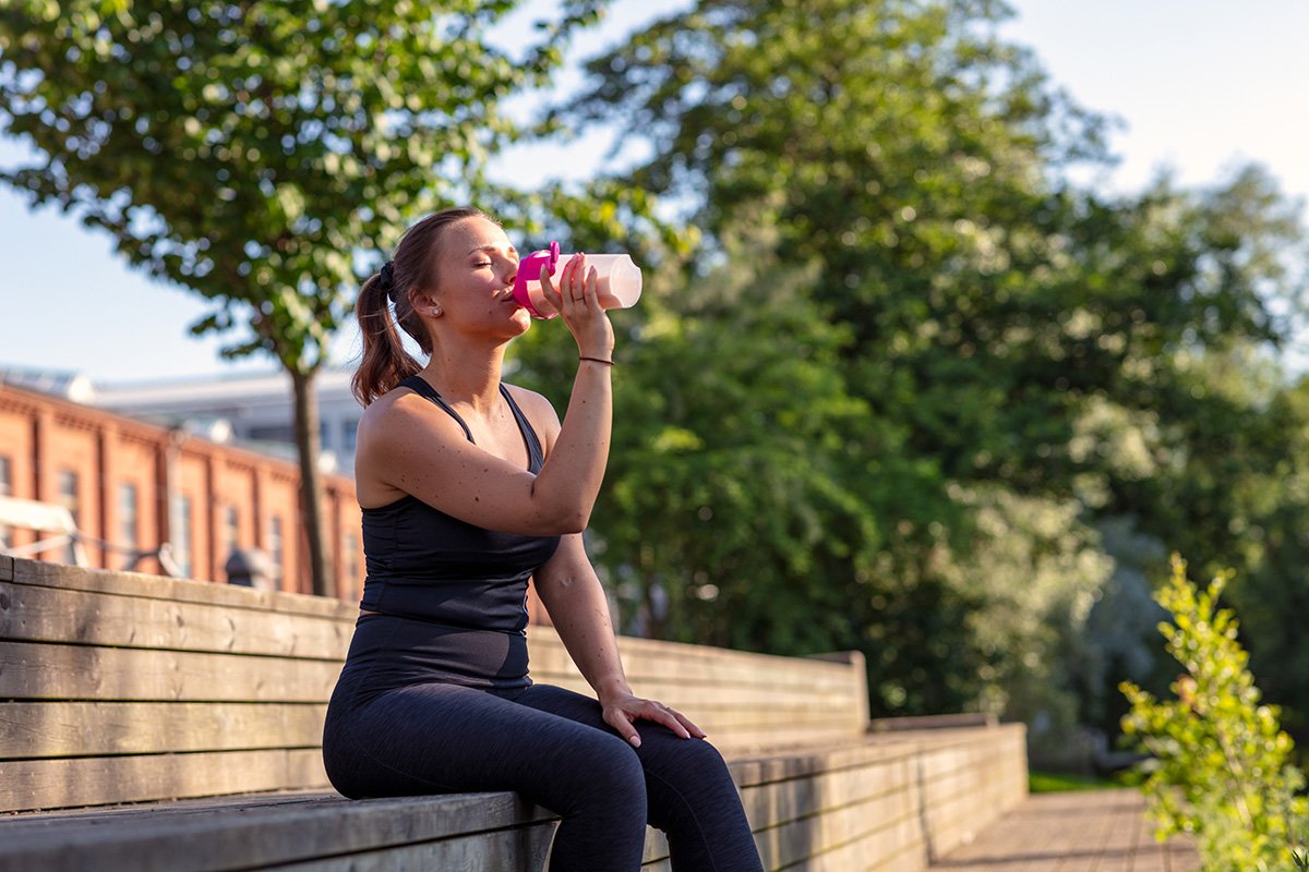  woman exercising outside drinking protein shake 