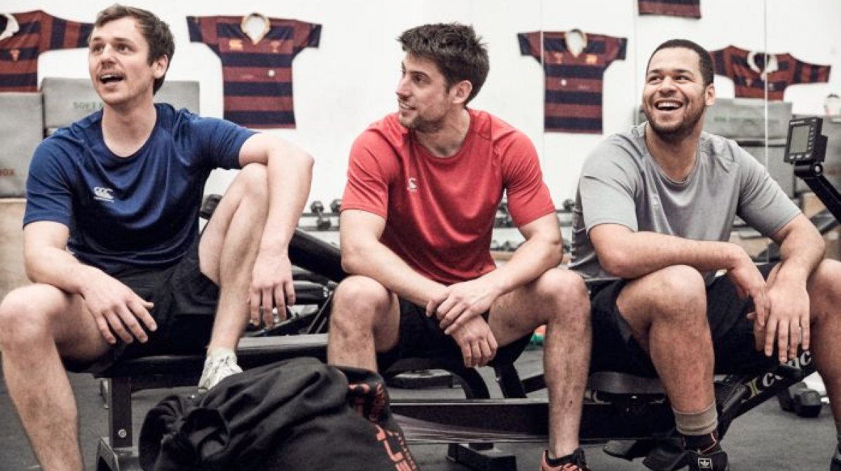 Three men sit on tyre in gym