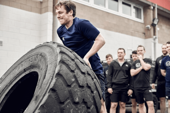 Man flips tyre with team cheering behind him