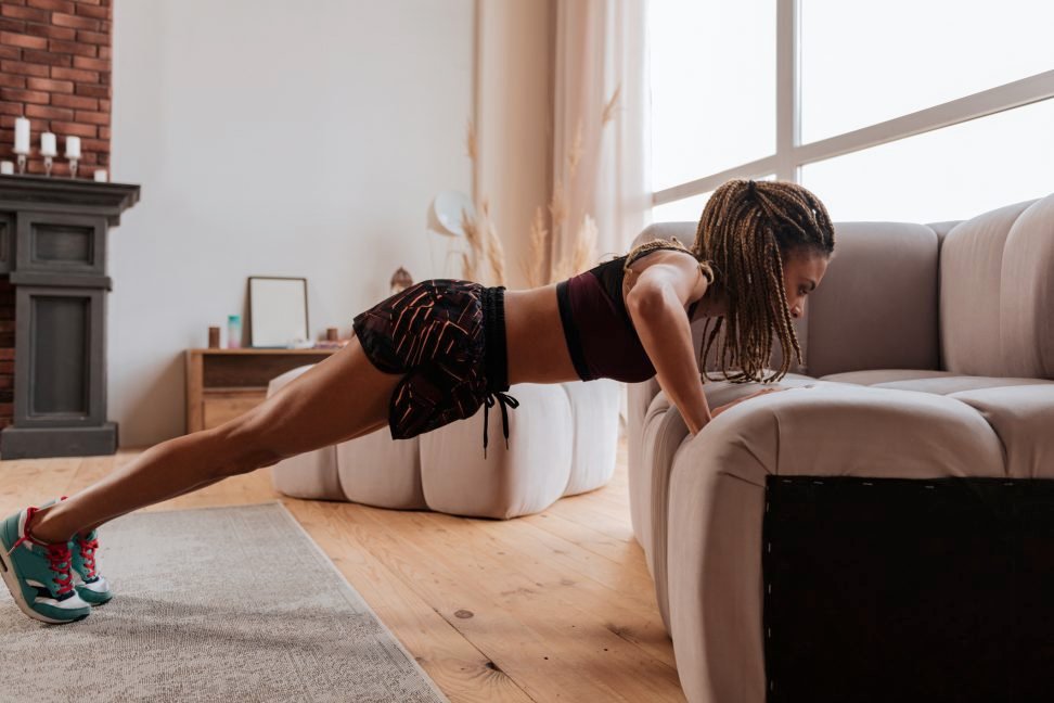 Woman performs sit up with hands placed on couch