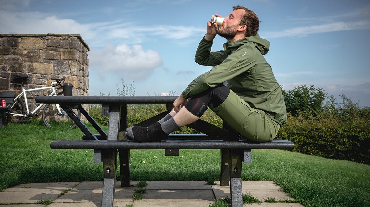 Man drinks coffee sat on Bench in Green Endura waterproof