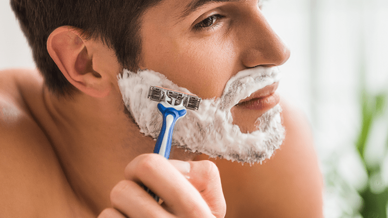 man shaving face with razor 