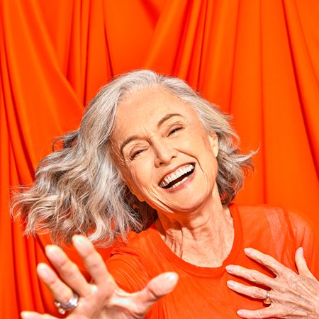woman with grey hair smiling at the camera with a red background