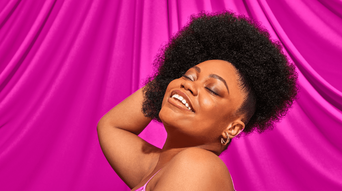 women stood in front of a pink background with an with an afro smiling