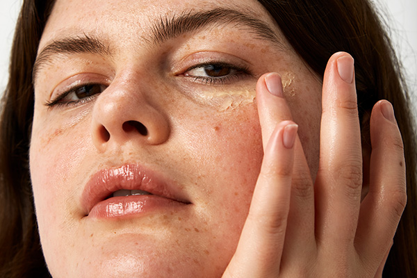 a close up image of a female model layering on her skincare, in a studio setting, in front of a white background.