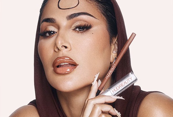A close up photograph of Huda Beauty founder, Huda Kattan, wearing a full face of glamourous make up and long nail extensions