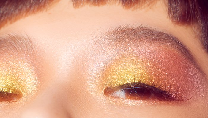 Woman wearing gold, sparkly eyeshadow. Close-up shot of eyes.