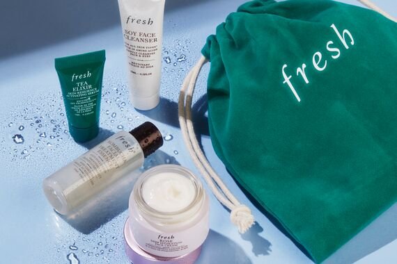 A flat lay of a mix of fresh skin care products with a green fresh drawstring bag on the side on a blue background with water splashes.