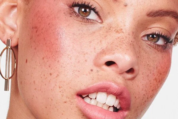 Freckled faced woman wears intensely pink blush while natural skin hues peak through make up. 