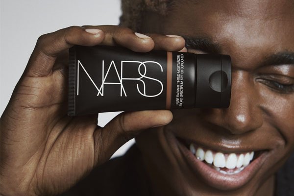 dark skinned male model holding onto a nars tinted moisturiser to his face