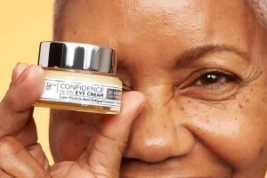 medium skinned older woman holding an it cosmetics eye cream hiding one eye