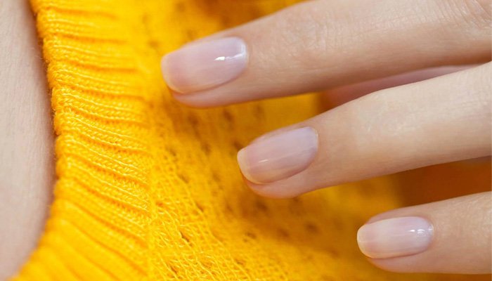 A close up shot of a model with painted, glossy nails layering her hand on a chunky knitted yellow jumper.