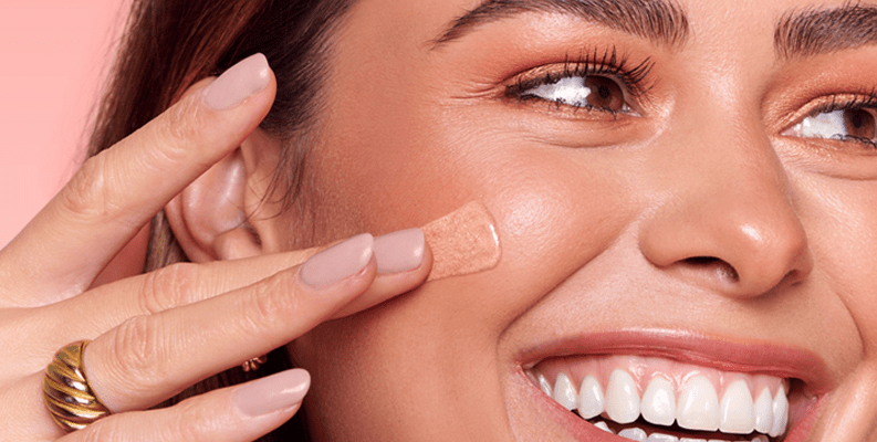 Model smiling and applying foundation to her cheek