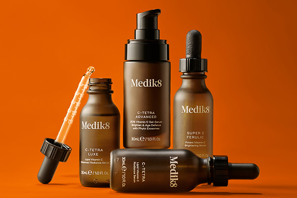 a collection of medik8 vitamin c serums shot against an orange background