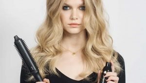 model with curled hair holding the ghd hot brush