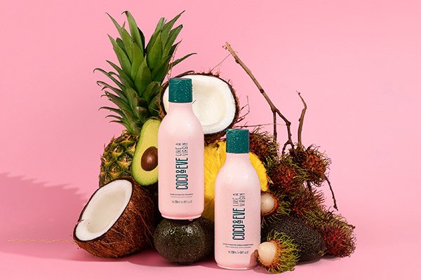 Two coco and eve bottles surrounded by coconuts and pineapples against a pink background