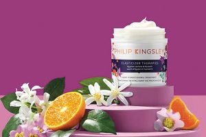 A JAR OF PHILIP KINGSLEY HAIR CARE SURROUNDED BY ORANGES AND FLOWERS