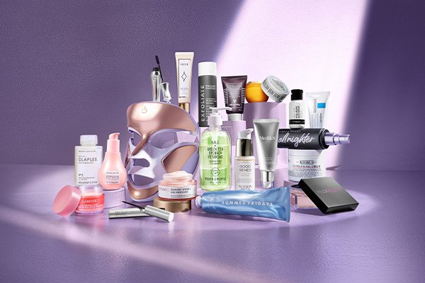 A full collection of beauty products, including skin care, body care and make up, shot in a studio with a light lilac background