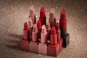 a collection of huda beauty lipsticks all open showing their shades from nude to red. shot against a glittery background in the studio