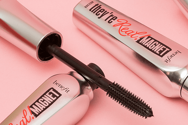 Two of Benefit’a They're Real Mascaras, one opened and one closed, in a studio setting on a pale pink background at an angle.