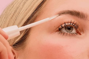 model applying brow serum to her thick eyebrow