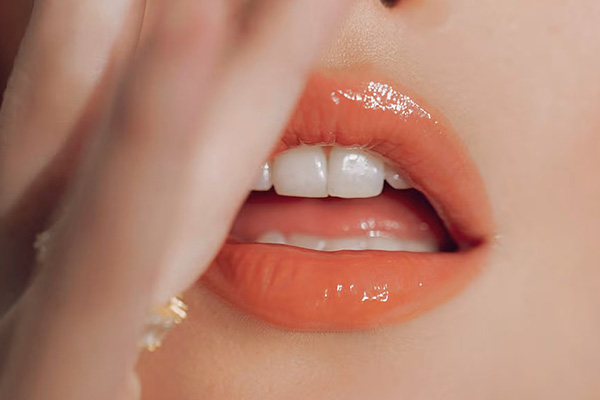 image of orange glossed lips on a fair skinned model her hand is slightly covering her mouth