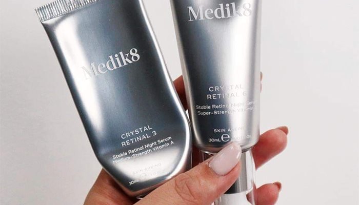 A medium shot of hands holding onto two bottles of Medik8’s Crystal Retinal serums in strength 3 and strength 6 in front of a white background.