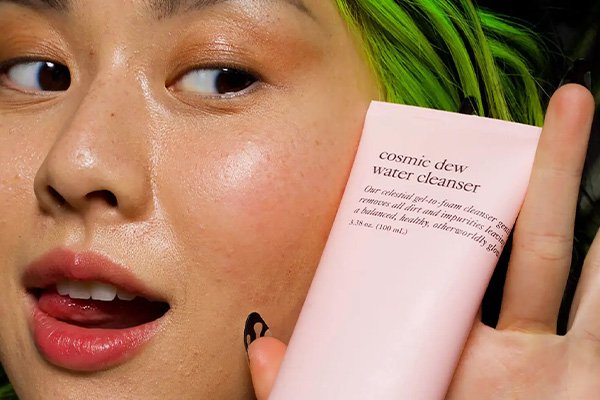 asian model holding a good light cleanser, she has green hair and is sticking her tongue out with super dewy skin