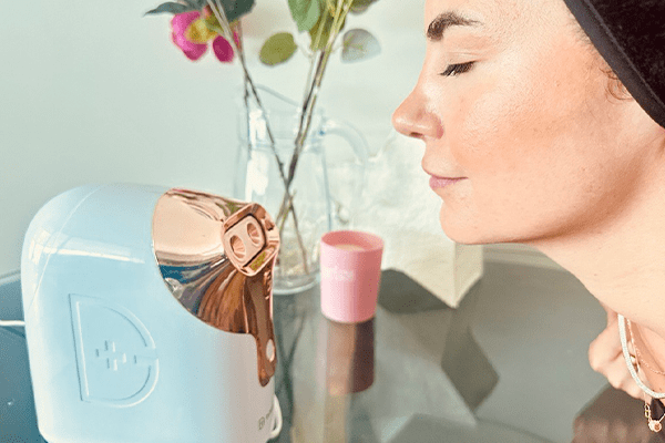 model wearing a black headband steaming her face with a vase of flowers and a candle in the background