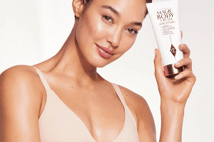 a tanned model with glowy skin holding charlotte tilburys magic body cream
