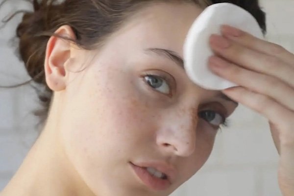 Woman swiping facial toner over face in bathroom setting 