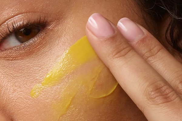 a medium skinned model applying a yellow coloured serum to her cheek