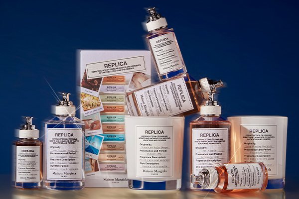 A medium shot of Maison Margiela’s REPLICA range including candles, fragrances and discover sets in a studio setting with a dark blue background.