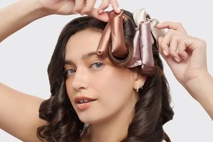 A model looking straight on, adding silk heatless curling rods into her hair in a studio setting with a white background.