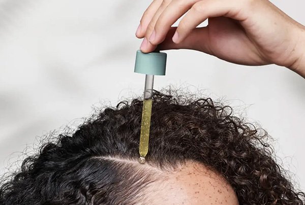 Model with curly hair applies Aveda's Scalp Solutions Overnight Scalp Renewal Serum