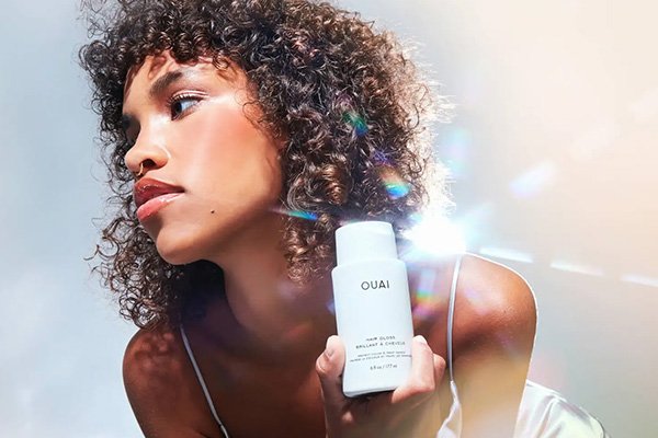 medium skinned model with afro hair looking off to the side a bright light behind her while shes holding ouai's hair gloss bottle