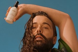 jonathan van ness holding a product with his right hand over his head