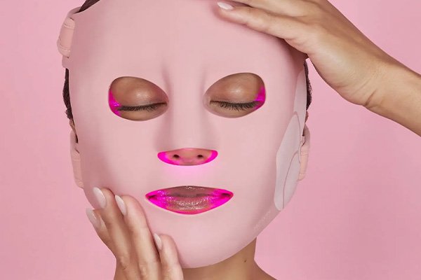 pink background with a model holding a pink LED MASK TO HER FACE