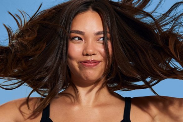 A medium shot of a brunette, long hair model throwing with her hair in the hair, in a studio setting on a blue background.