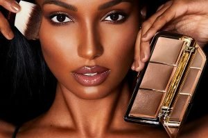a model holding the hourglass ambient light palette and a brush to her cheeks