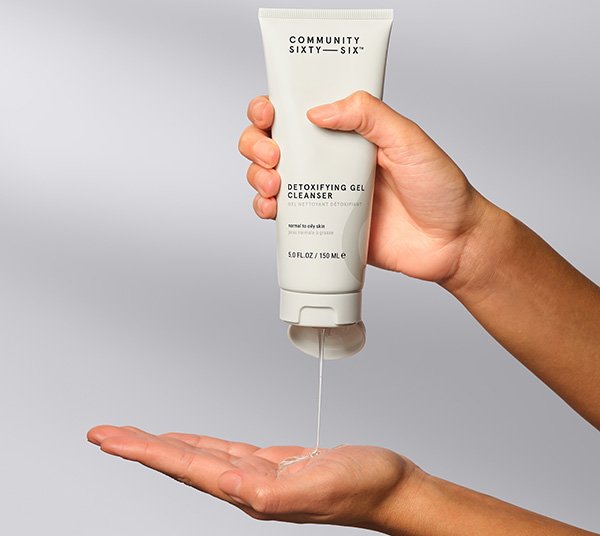 A wide shot of a models hands squeezing Community Sixty-Six’s Detoxifying Gel Cleanser into her hands on a grey background.